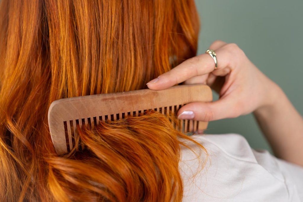 A person combing long red hair with a wooden comb, viewed from behind.